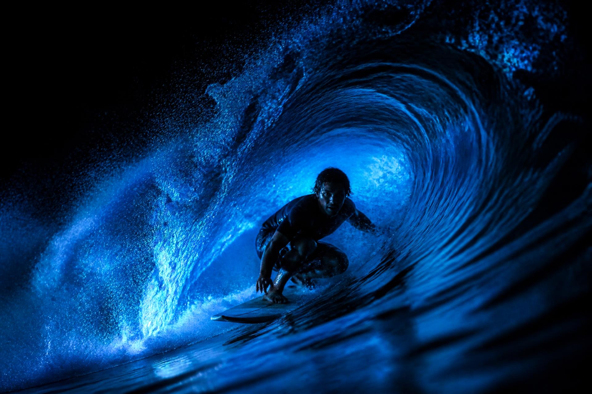Surfer riding inside a barrelling wave lit in electric blue